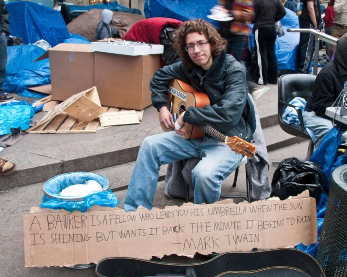 a young man sits with a guitar in the middle of a street