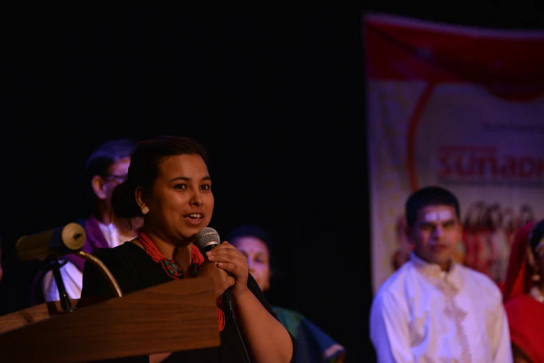 a woman speaks into a microphone as others watch