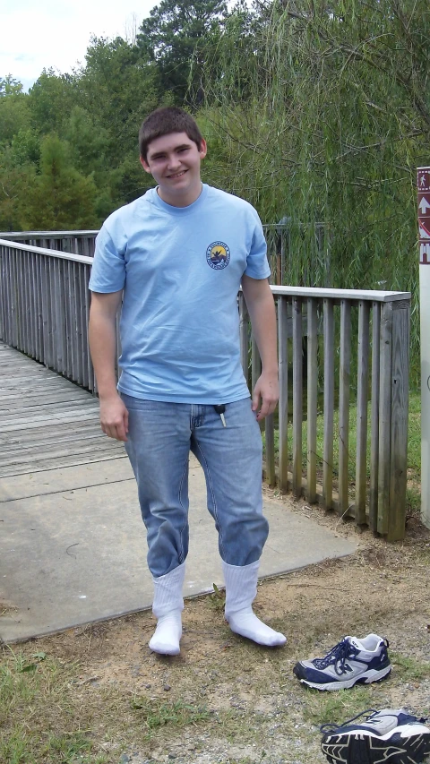 a man with blue shirt and jeans is standing on the ground near some shoes