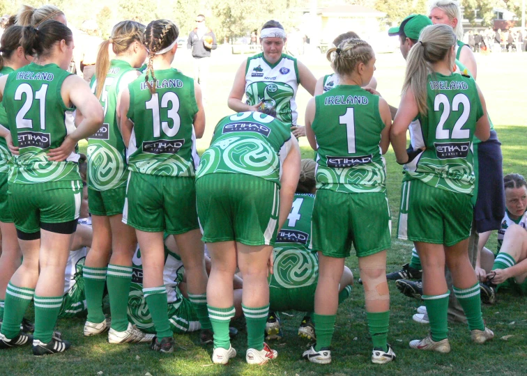 a group of girls in green jerseys stand in a circle