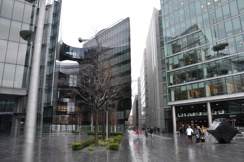 a rain soaked plaza next to a building with glass and stone front entrance