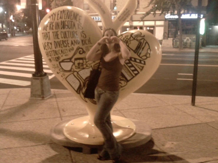 woman posing with large heart shaped sculpture on sidewalk