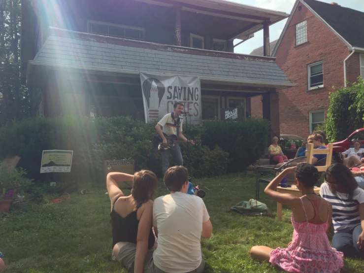 a group of people sitting on the grass outside of a house