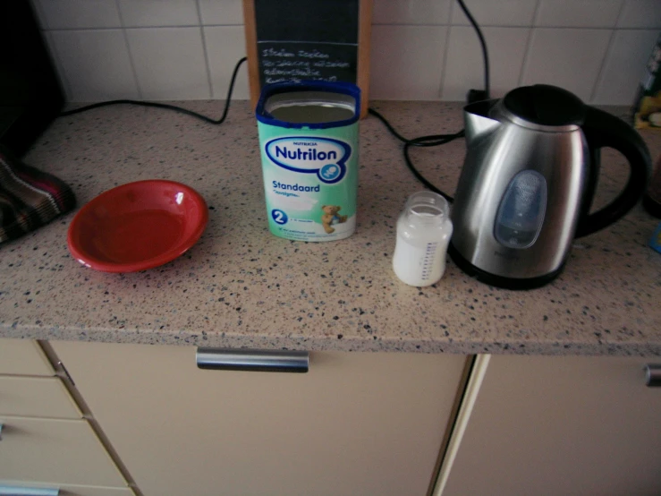 a blue and white tea kettle, a black and white coffee pot, a red plate with milk on it and a silver electric device