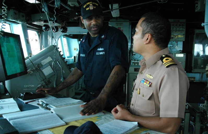 two sailors standing at a computer in a ship