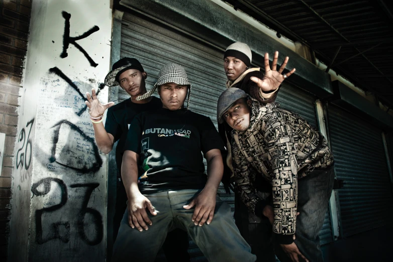 four young guys stand in front of graffiti covered building