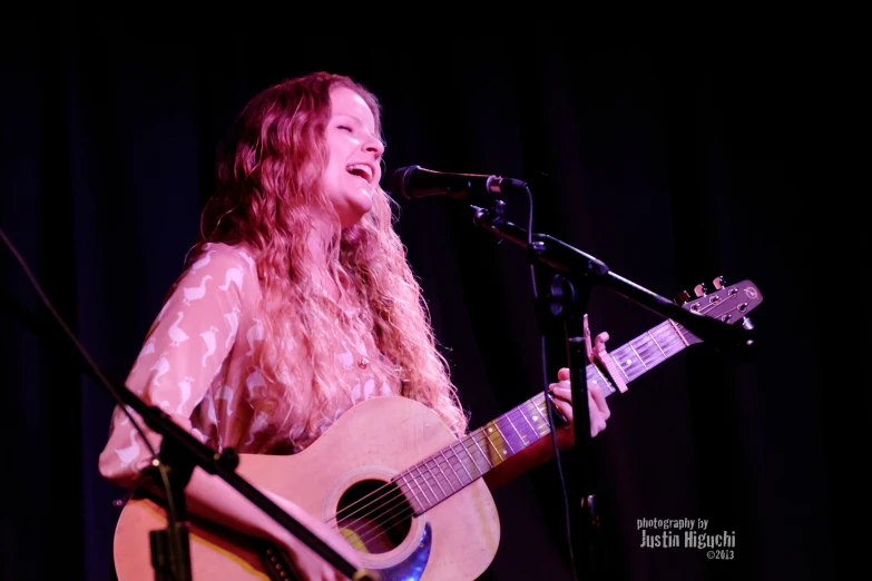 a woman singing into a microphone next to a guitar