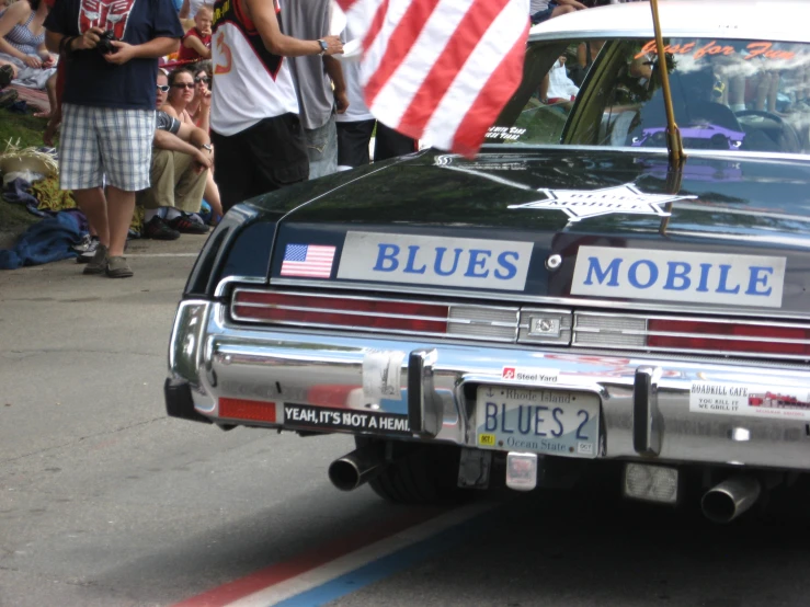 a classic car parked in the street with two american flags on the tail