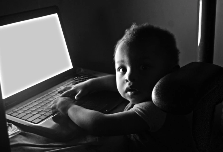 a toddler sitting in front of a laptop computer