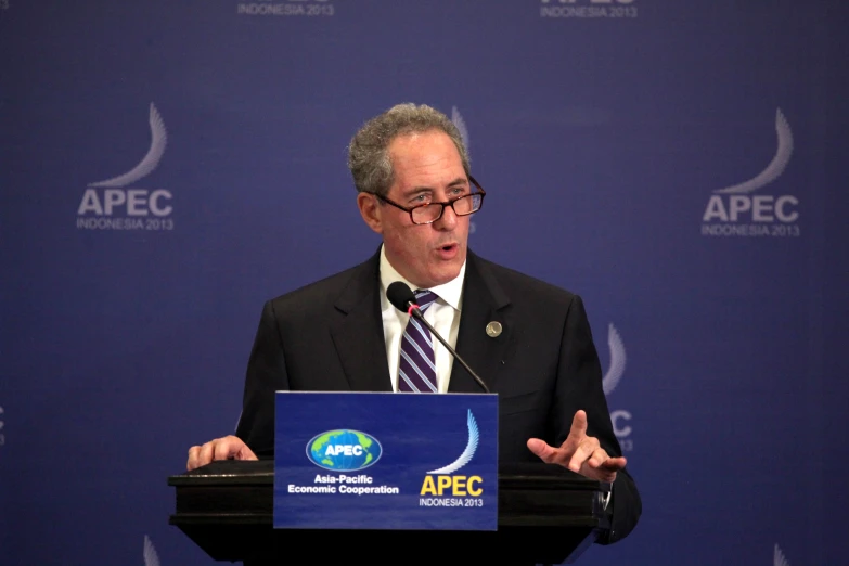 a man speaking at a podium with an apec sign behind him