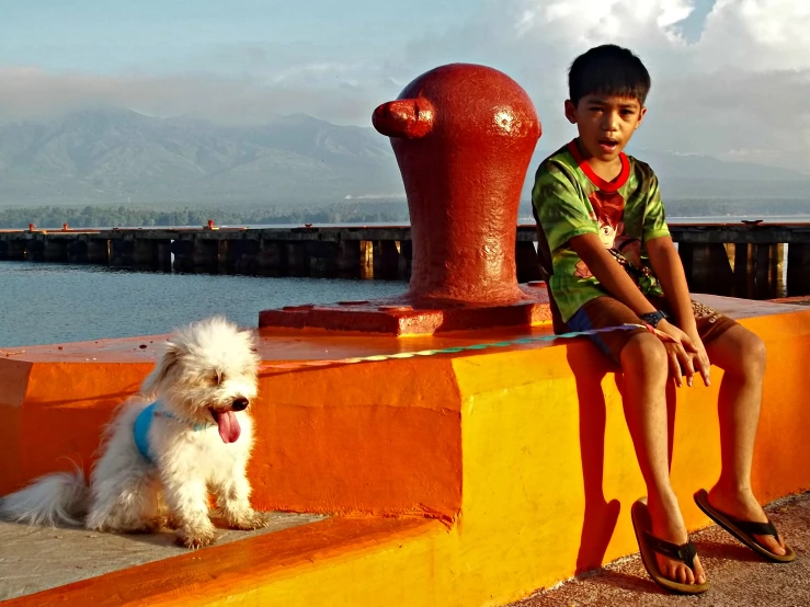 the small boy is sitting next to a small dog near a water pump