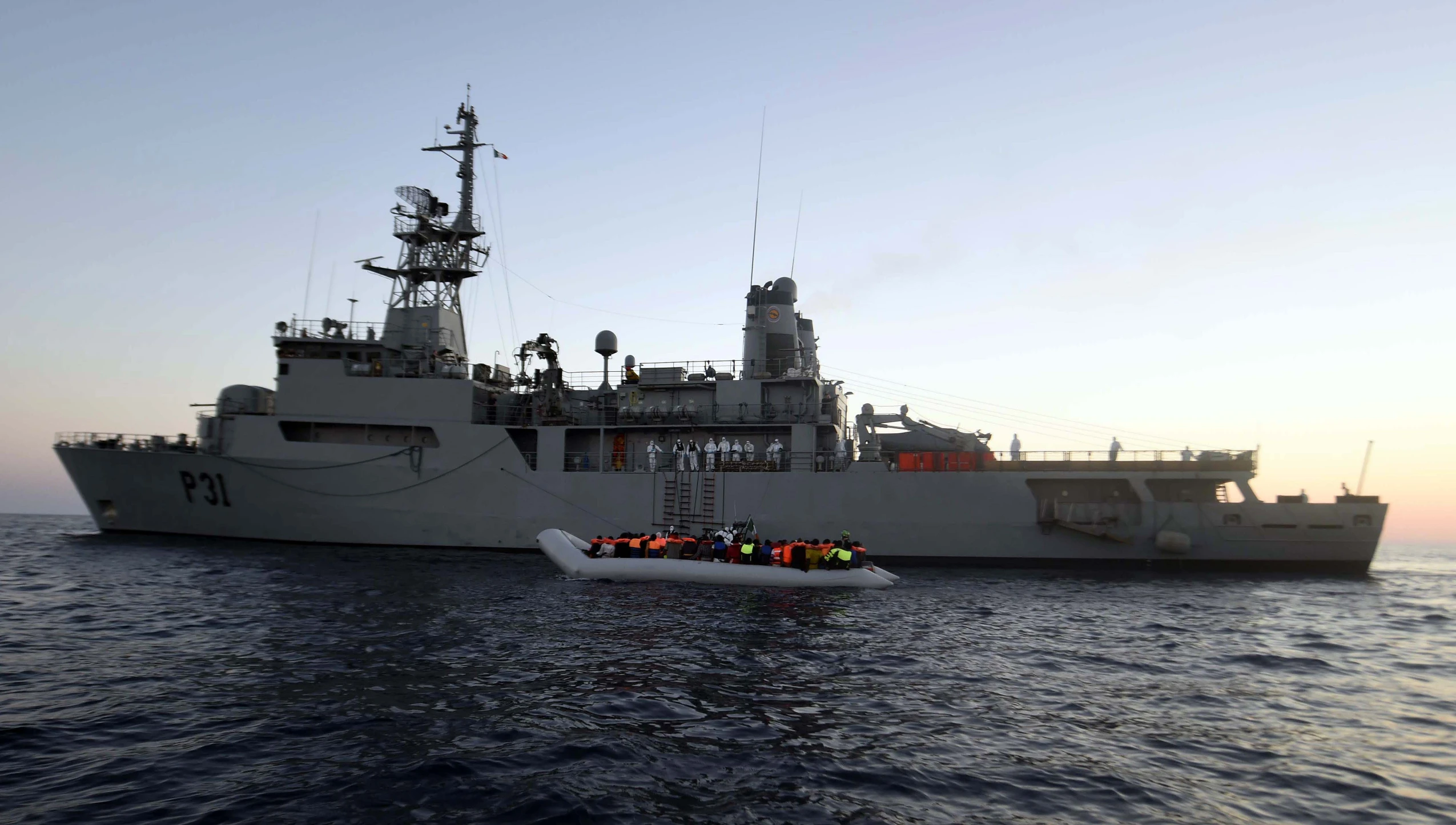 several people on an inflatable raft float by a large ship