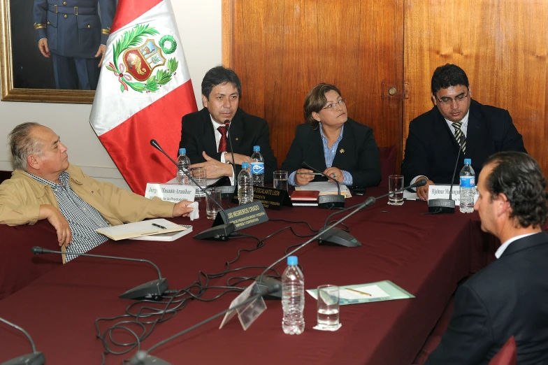 five business people sitting around a table with flags in the background