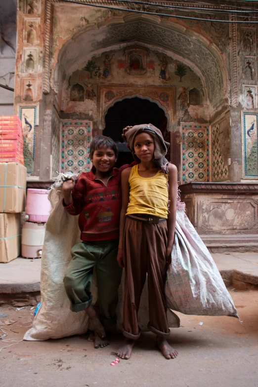 two young children standing together in front of a building with a large bag