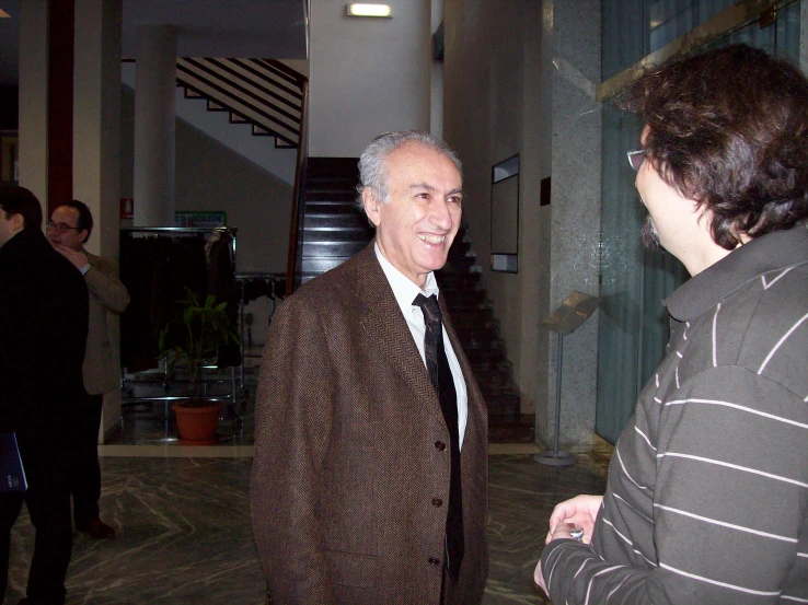 an old man wearing a jacket and tie talking to a woman