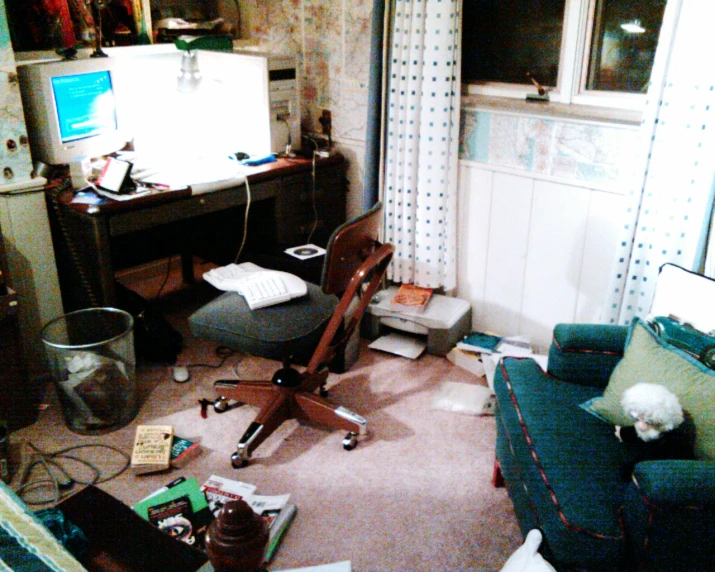 a messy living room with a desk and computer on the chair