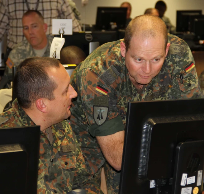 a man in camouflage standing next to another man with a computer