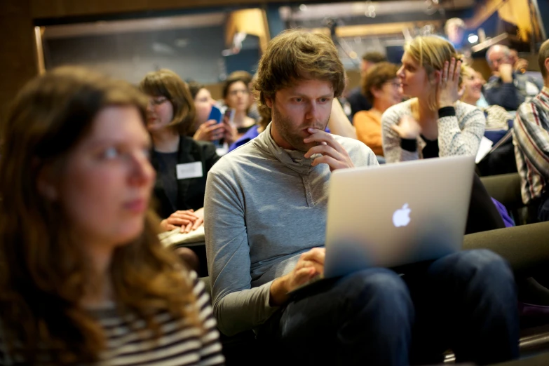 a man on a laptop looks confused while he is watching other people in chairs