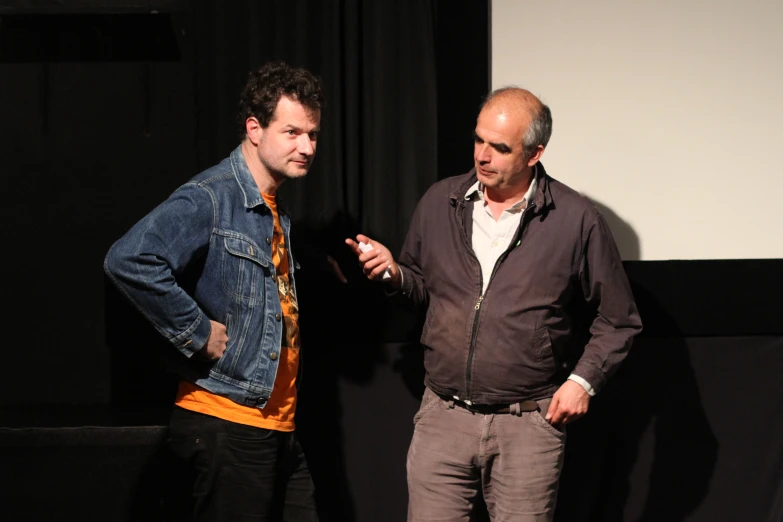 two men in denim jackets standing by a podium