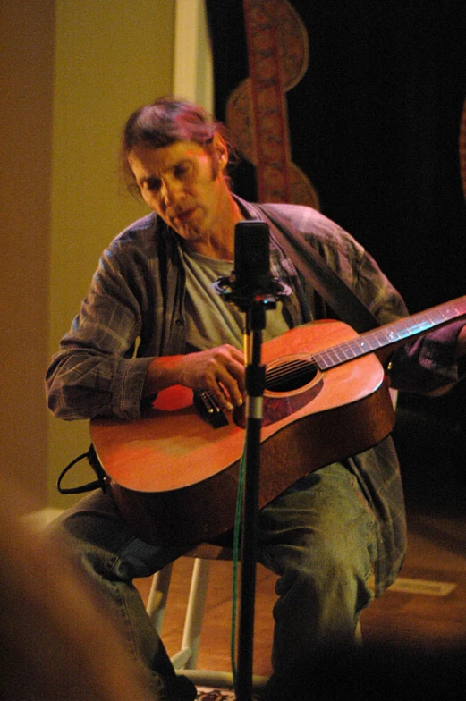 a man sitting in front of a microphone and playing guitar