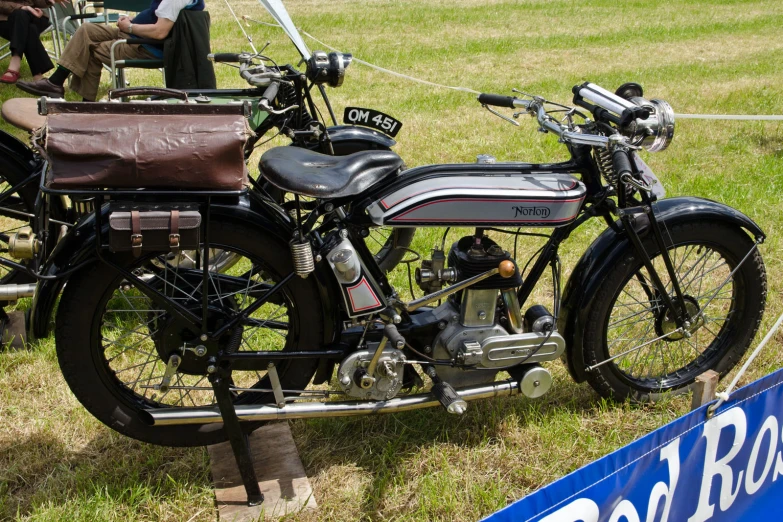 an old fashion motorbike sits in the grass with people