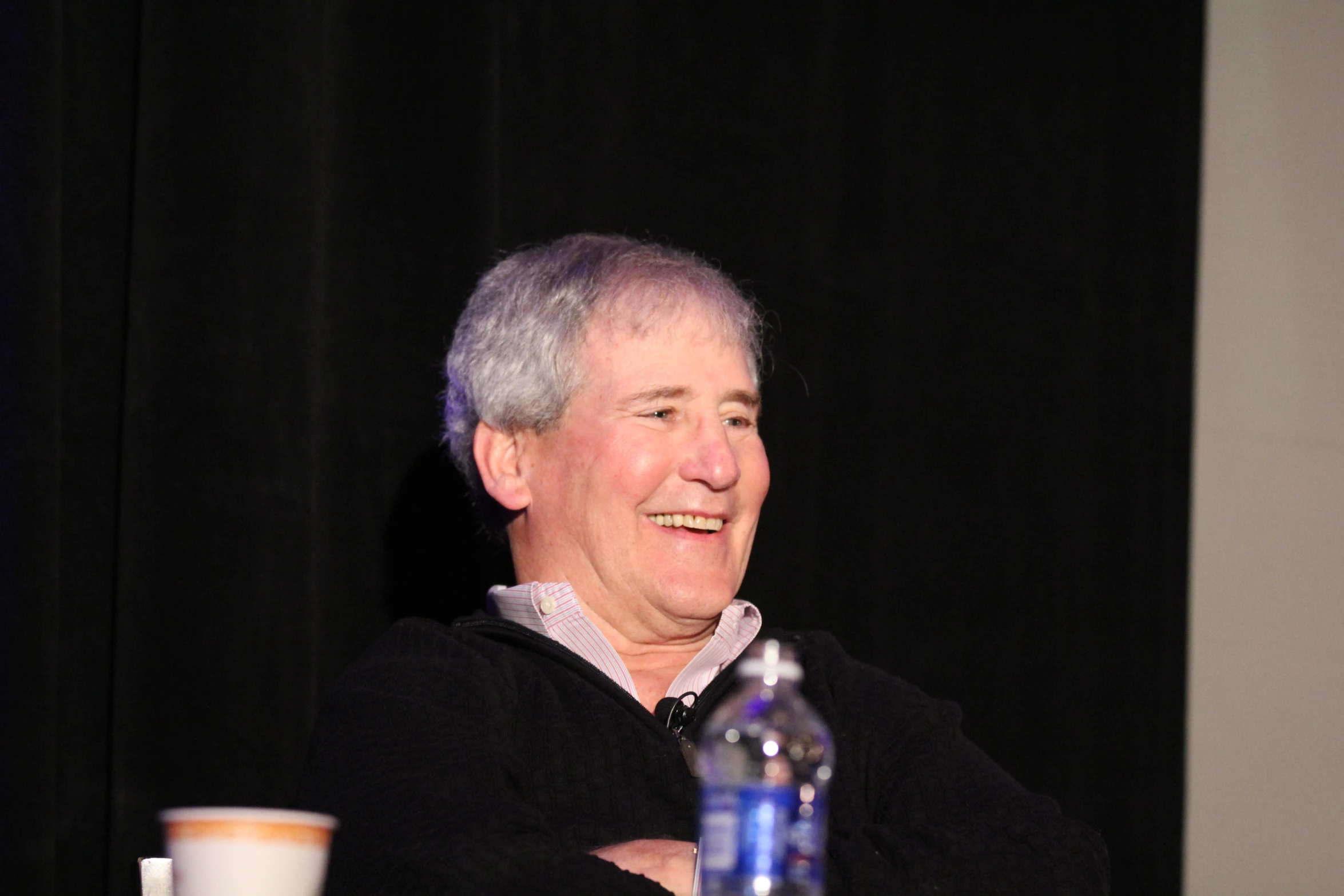 a man with his arms folded standing in front of a black curtain