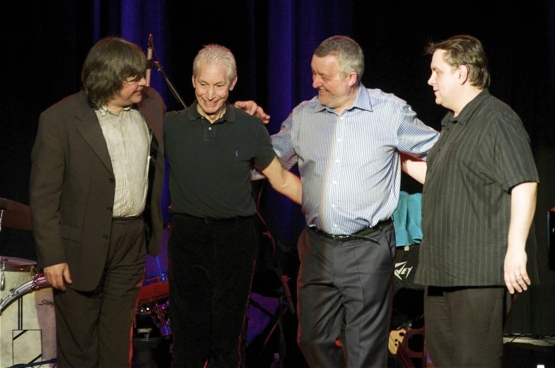 three men and one man stand by a microphone