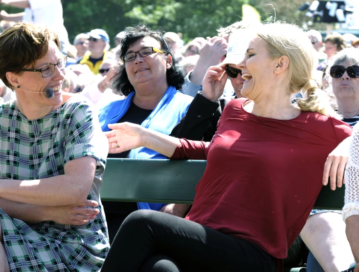 an old woman with glasses talks to a young lady sitting in the stands at a park