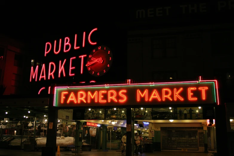 large, colorful neon sign at night with public market in background