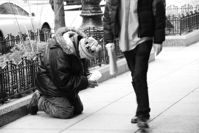 a person with hair covered in a jacket kneeling down next to a street