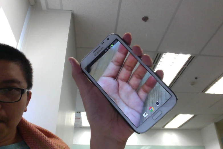 man holding up samsung smartphone with picture of an object on screen