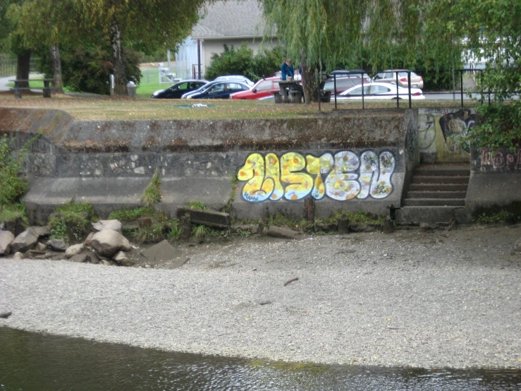 graffiti written on the side of a concrete wall by the water