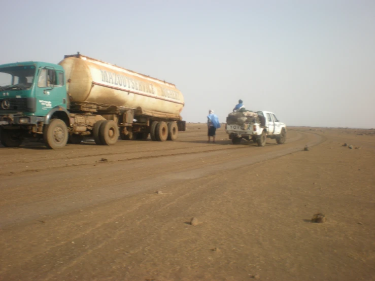 two trucks that are on the road near some people