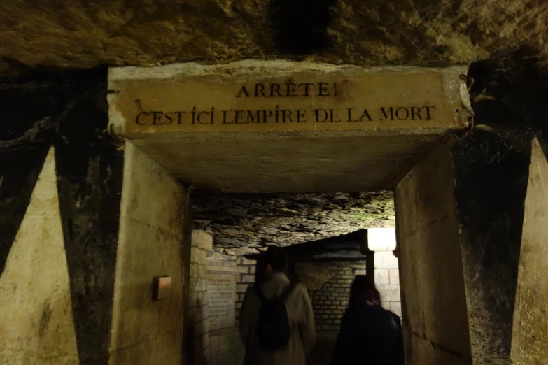 two people walking through the tunnel leading to some sort of structure