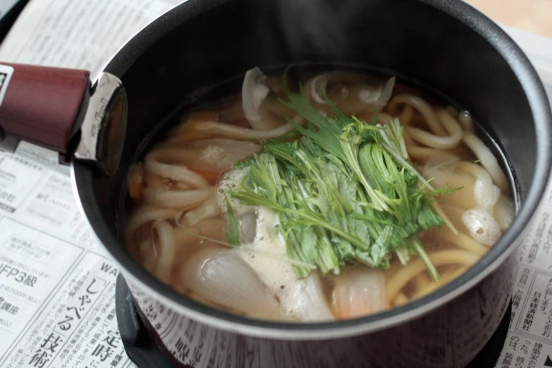 a pot of noodle soup with herbs on top of it