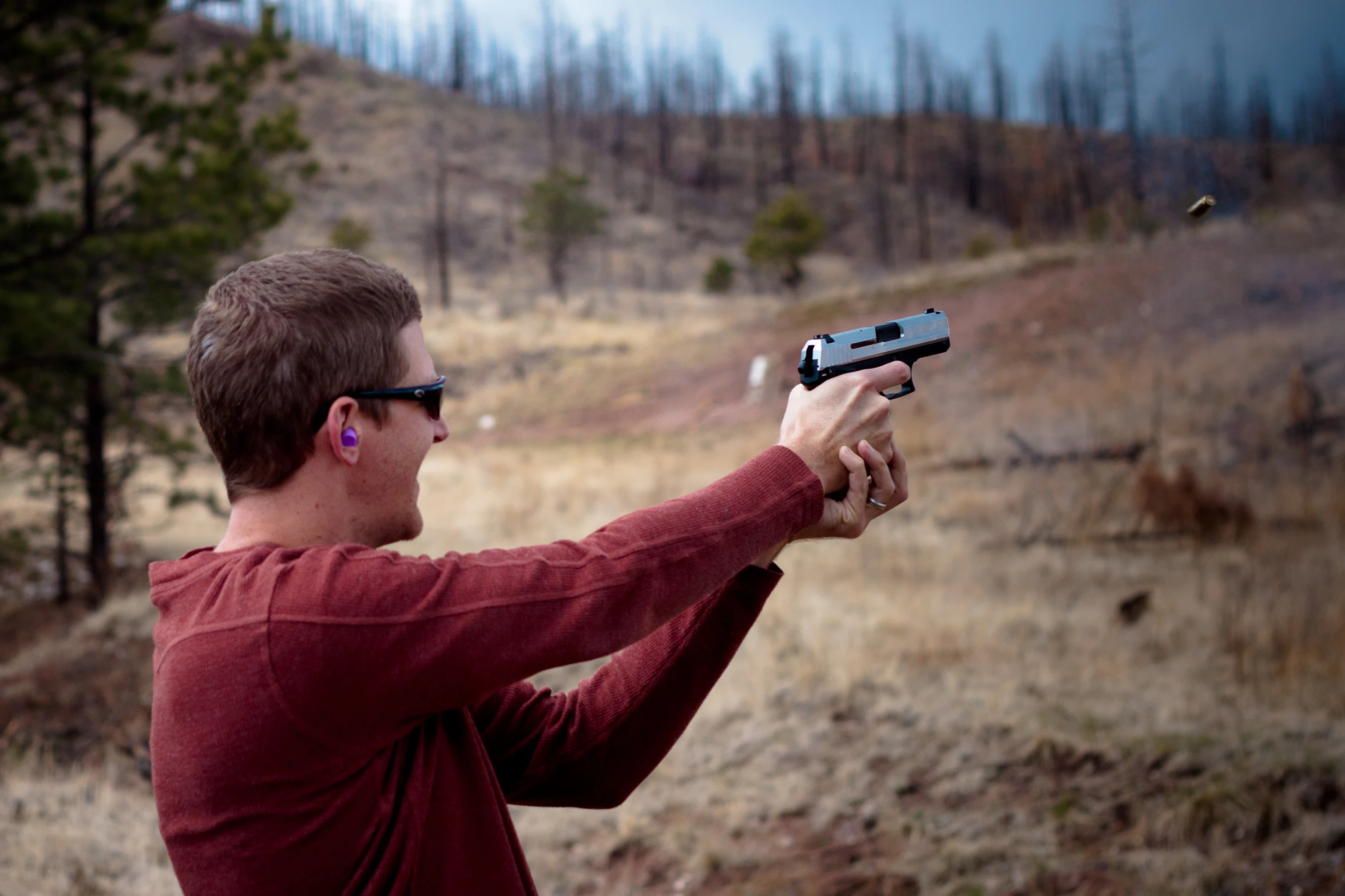 a man with glasses aiming at a rifle