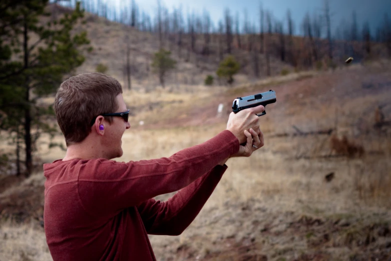 a man with glasses aiming at a rifle