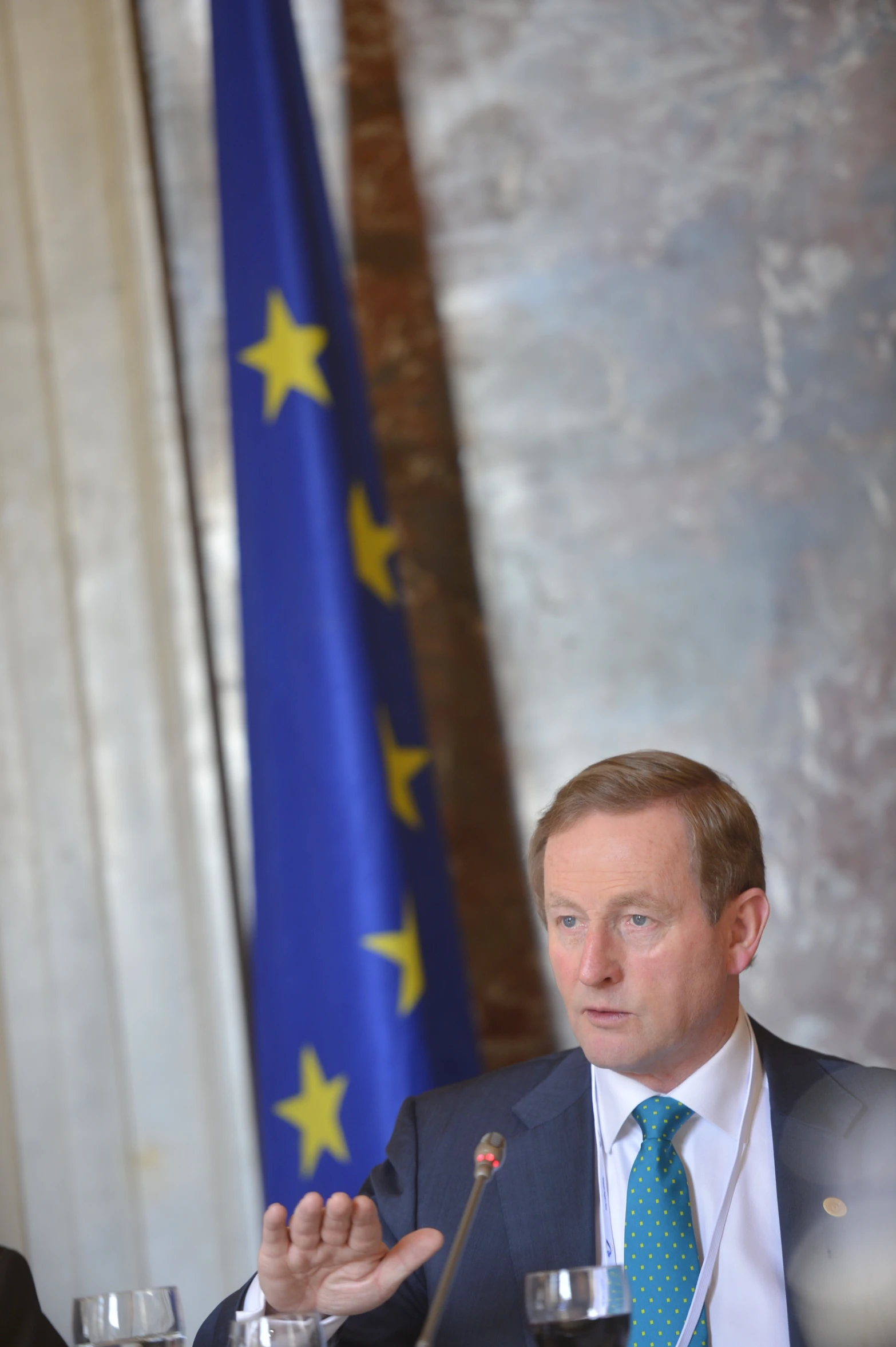 two men in suits are speaking in front of flags