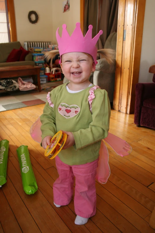 a toddler wearing a pink princess crown on her head standing in a living room