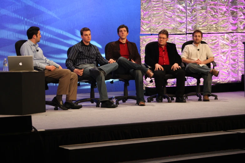 six people are sitting around a stage on laptop computers