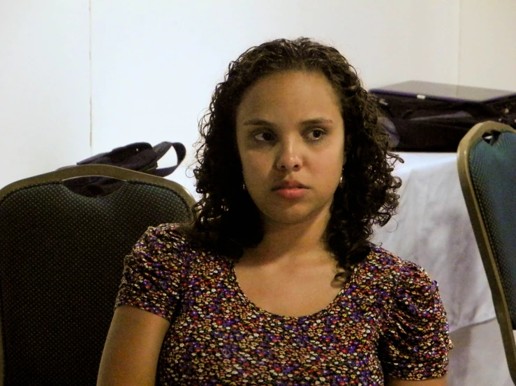 a woman with dark curly hair sits by a table