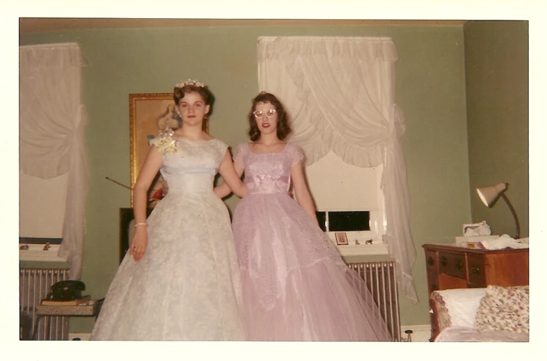 two women in dresses are standing near a wall