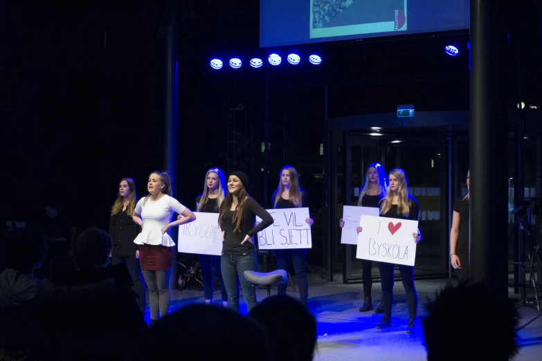 four woman holding signs on stage during a presentation