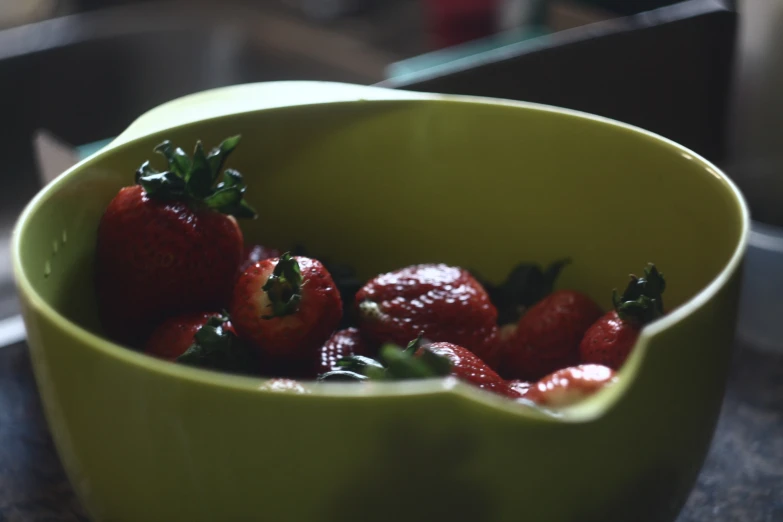 a green bowl full of strawberries sitting on top of a counter