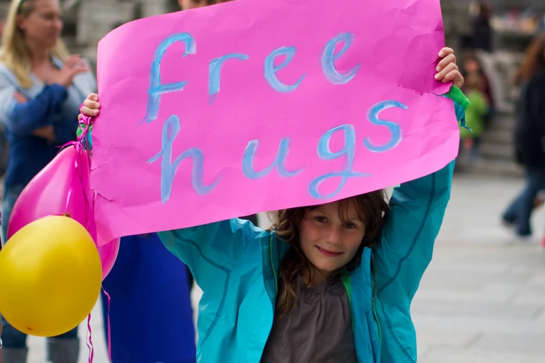 a girl holding a free hugs sign and holding balloons