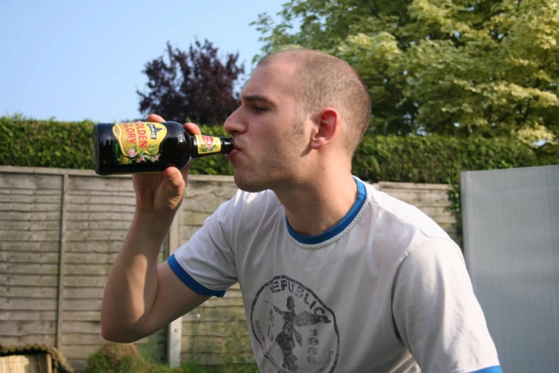 a man drinks a beer while standing in front of a garden
