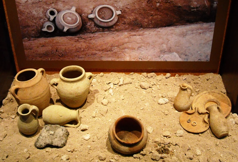 various pottery pieces displayed on sand beneath a painting