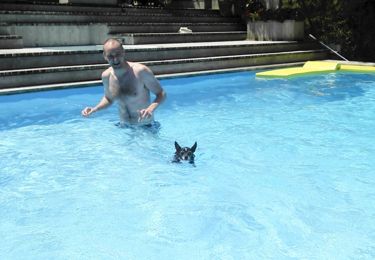 a shirtless man with his dog playing in the swimming pool