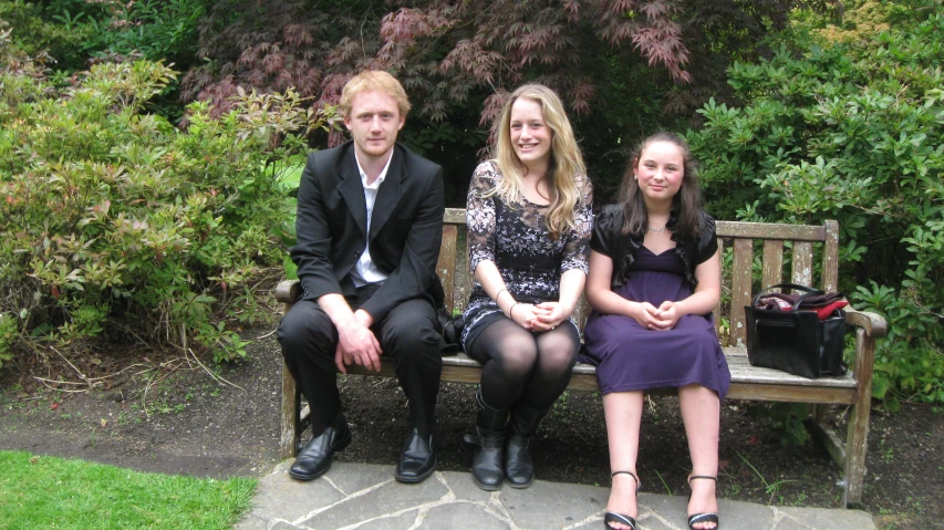 a man and two women on a bench near some bushes