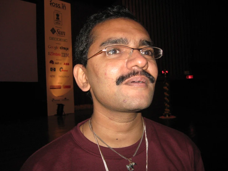 an indian man in a red shirt wearing glasses and necklace